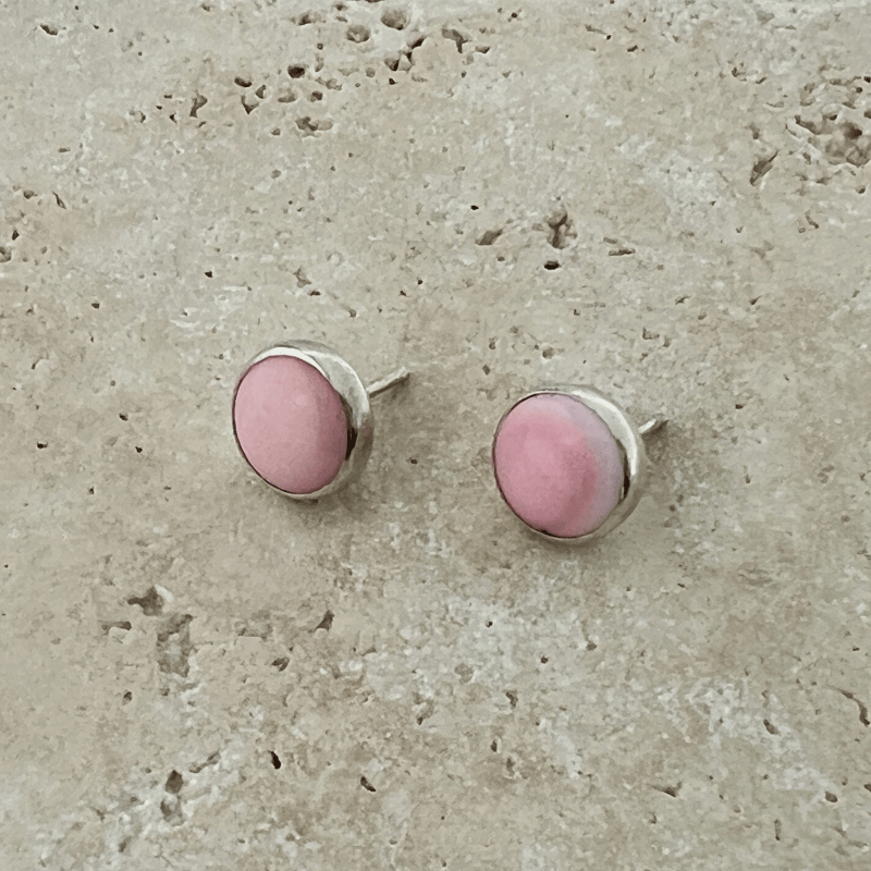 Close-up of pink conch shell stud earrings set in polished sterling silver bezels on a natural stone background.