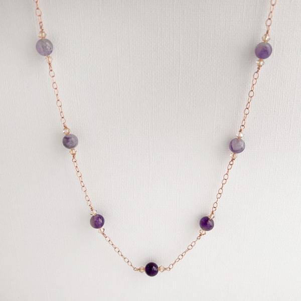 Make a glamorous statement with this stunning ombré-style necklace featuring natural Amethyst gems, Swarovski crystal golden shadow beads, and a 14Kt rose-gold filled chain. The unique design adds a flowing ombré pattern that captivates the eye. Perfect to add a touch of elegance to your everyday wardrobe. Modeled with matching earrings and a single pearl on a rose gold chain choker.