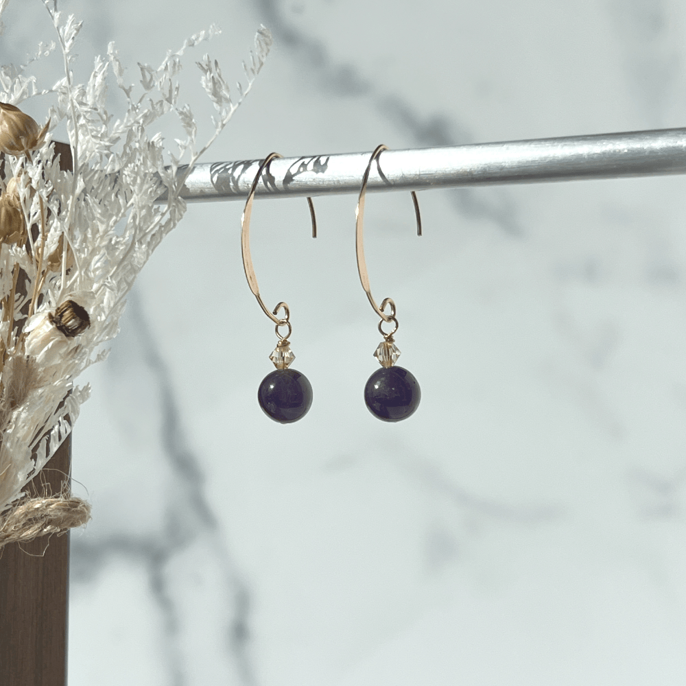 These elegant Amethyst earrings from our collection promise to make a chic statement wherever you go. The flat V-shaped half-hoop ear wire is crafted from 14Kt Rose Gold-filled metal, and each earring is adorned with a shimmery golden Swarovski crystal bead.