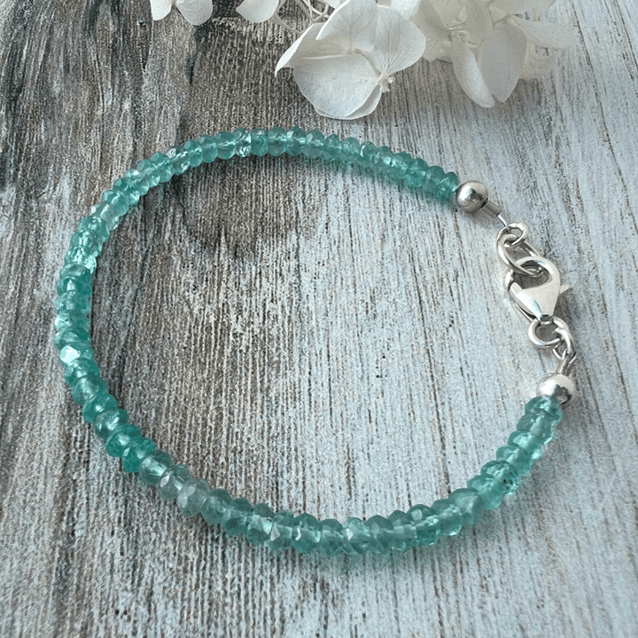 Teal Apatite gemstone beaded bracelet with a sterling silver lobster clasp on a wooden surface.