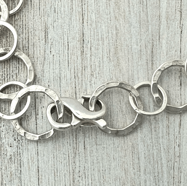 Close-up of the silver infinity clasp on the silver chain on a textured gray background