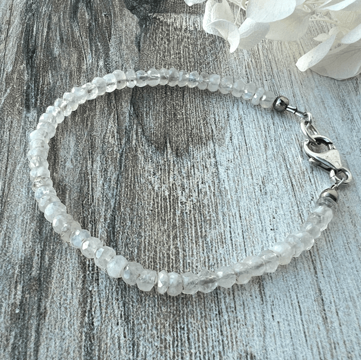 Rainbow Moonstone Beaded bracelet with a sterling silver lobster clasp on a textured wood surface.