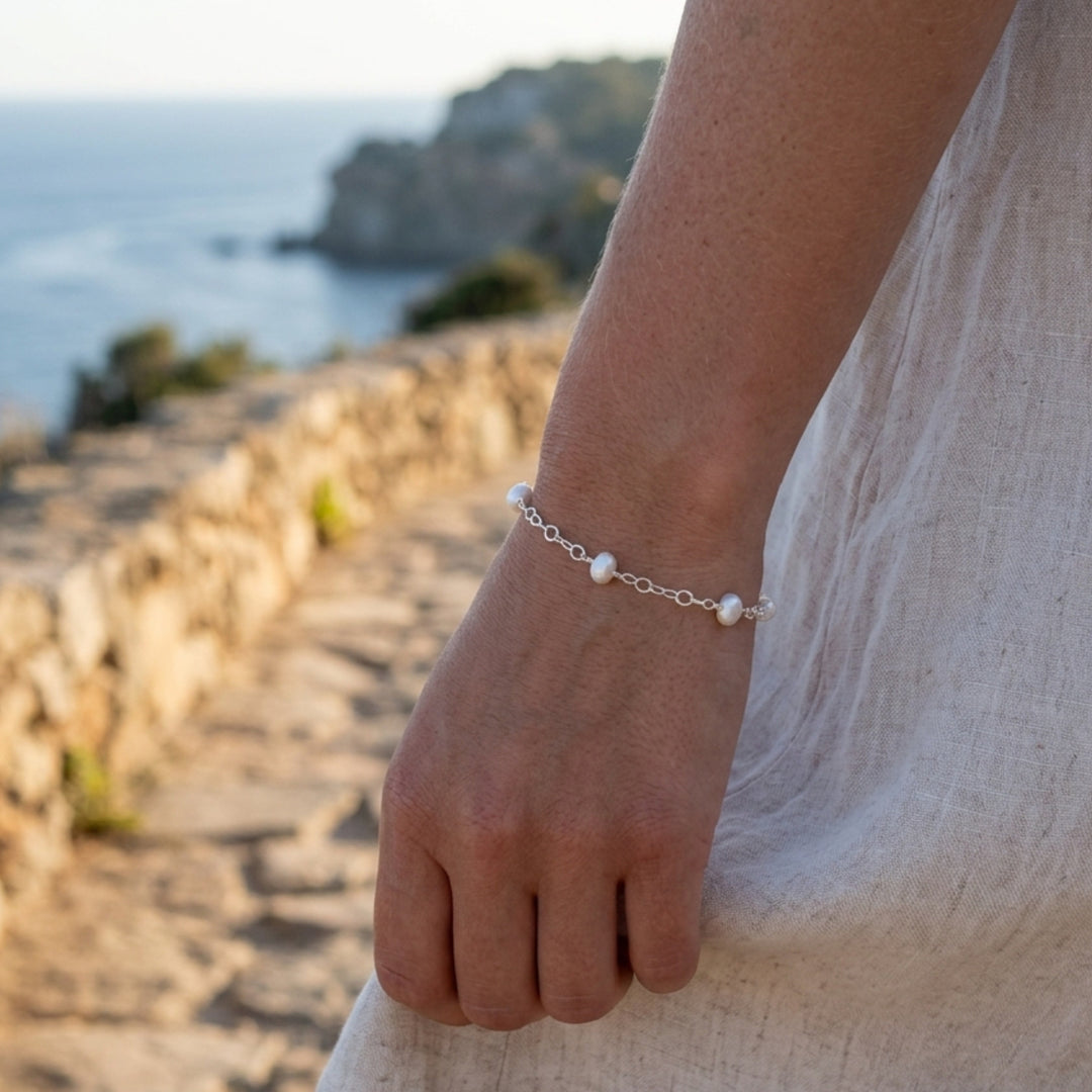 A woman is wearing a pearl and sterling silver bracelet with a coastal background of water and rocks.