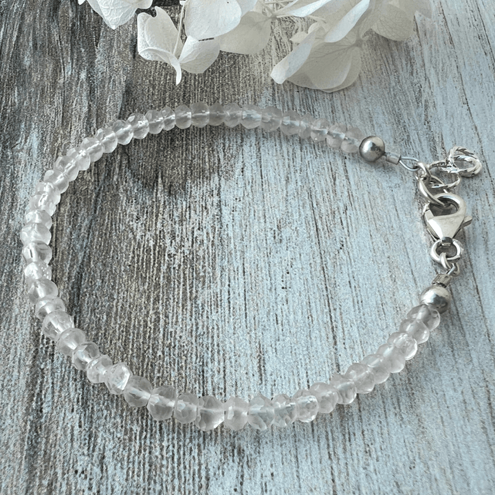 Rose Quartz beaded bracelet with a sterling silver lobster clasp on a textured wood surface.