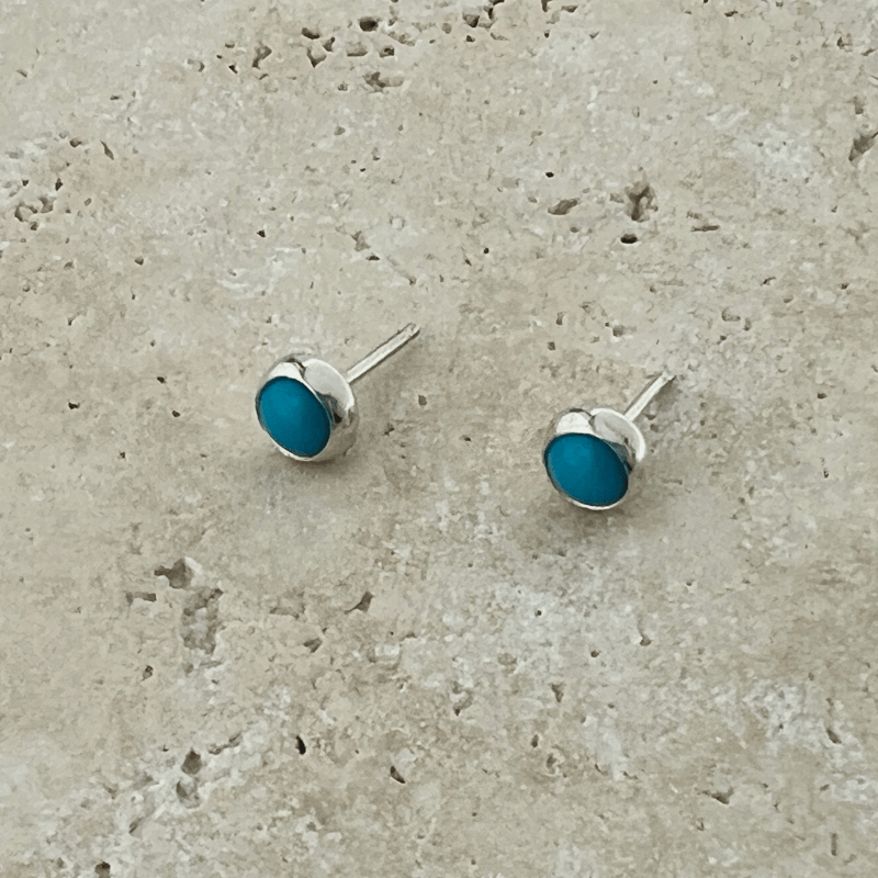 Close-up of Sleeping Beauty turquoise stud earrings set in polished sterling silver bezels on a natural stone background.