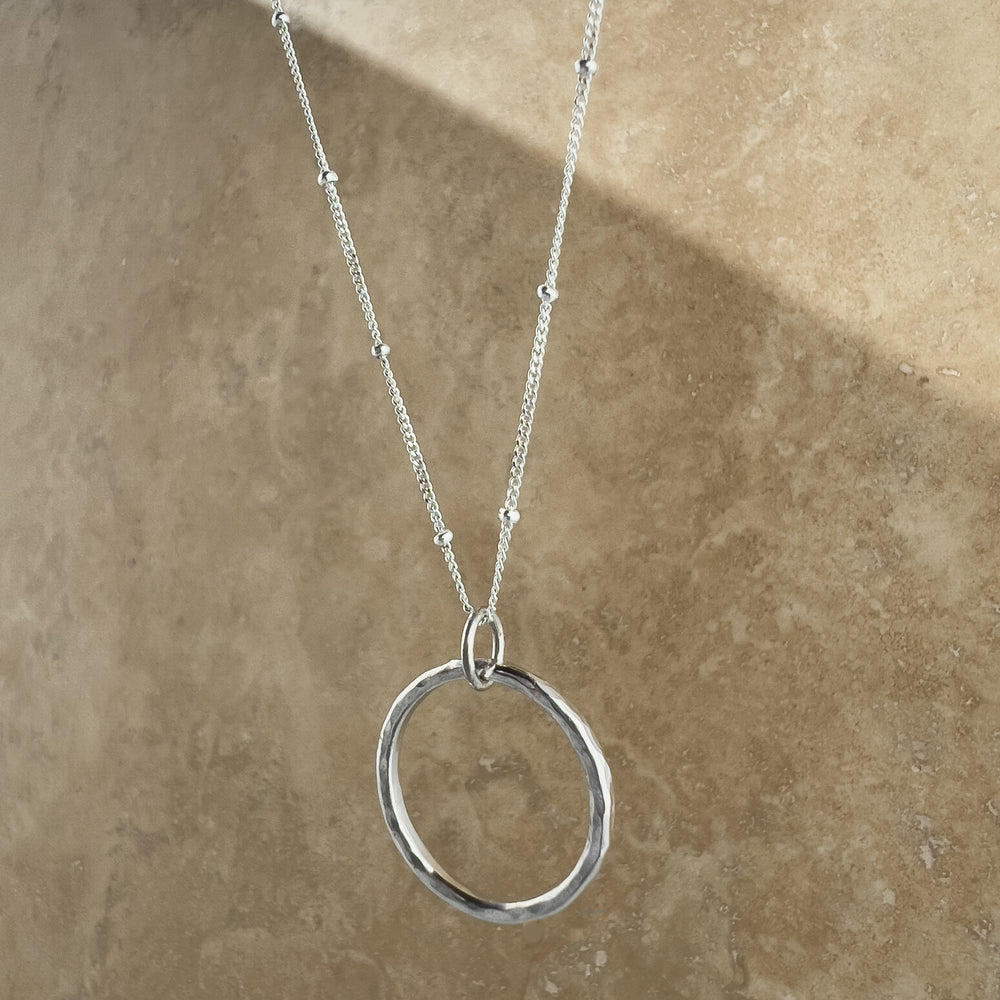 Circle Necklace. Made of sterling silver, this open-circle pendant features a stunning hand-hammered texture that reflects light. 