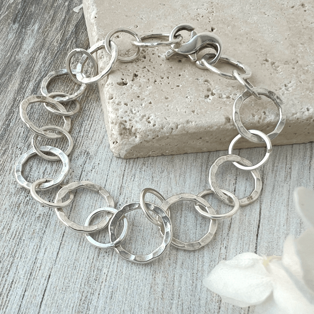 Close-up of fine silver link bracelet with hammered texture and infinity clasp, handcrafted by Hilltribes artisans on a natural stone background.